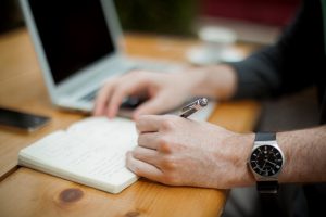 Hands writing and a laptop 618x412