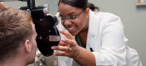 Female optometrist using a machine to examine the eyes of a teen boy.