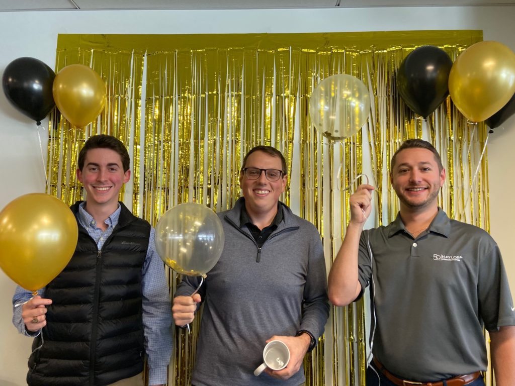 3 men standing in front of a gold curtain, holding balloons